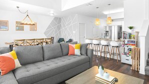 A modern living room with a grey sofa, wooden dining table, and bar stools.