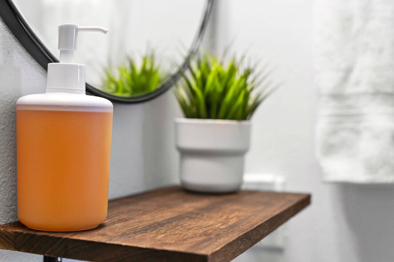 Een badkamer met een houten plank, een witte fles met pompje en een potplant.