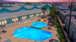 A hotel with a large outdoor swimming pool, sun loungers, and umbrellas.