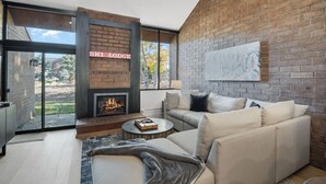 A modern living room with a fireplace, a sofa set, and a large window offering a view of the outdoors. - Park Avenue Condos by Park City Vacations (Park City)