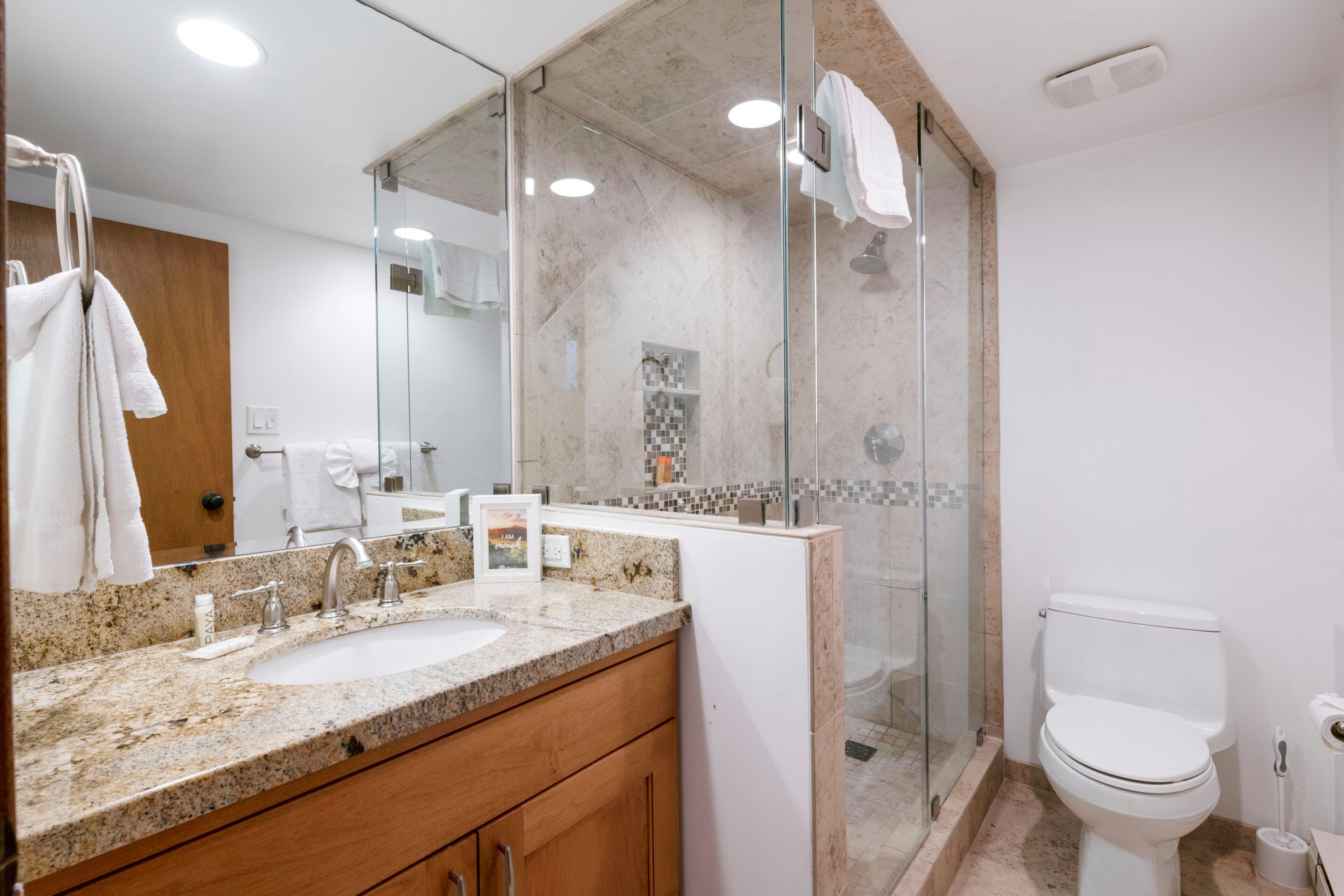 A modern bathroom with a granite countertop sink, a glass shower enclosure, and a white toilet.