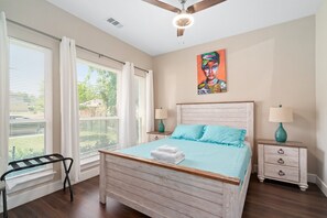 A bedroom with a wooden bed, two bedside tables with lamps, a ceiling fan, and a window with curtains.