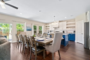 A modern kitchen with wooden cabinets, a dining area with a table set for six, and a view of the outdoors.