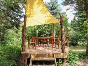 Una terraza de madera con una mesa y sillas, rodeada de árboles.