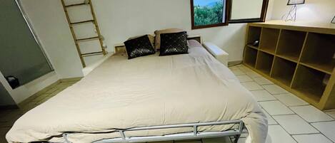 A bedroom with a bed, pillows, a ladder, a window, and a desk with a lamp.