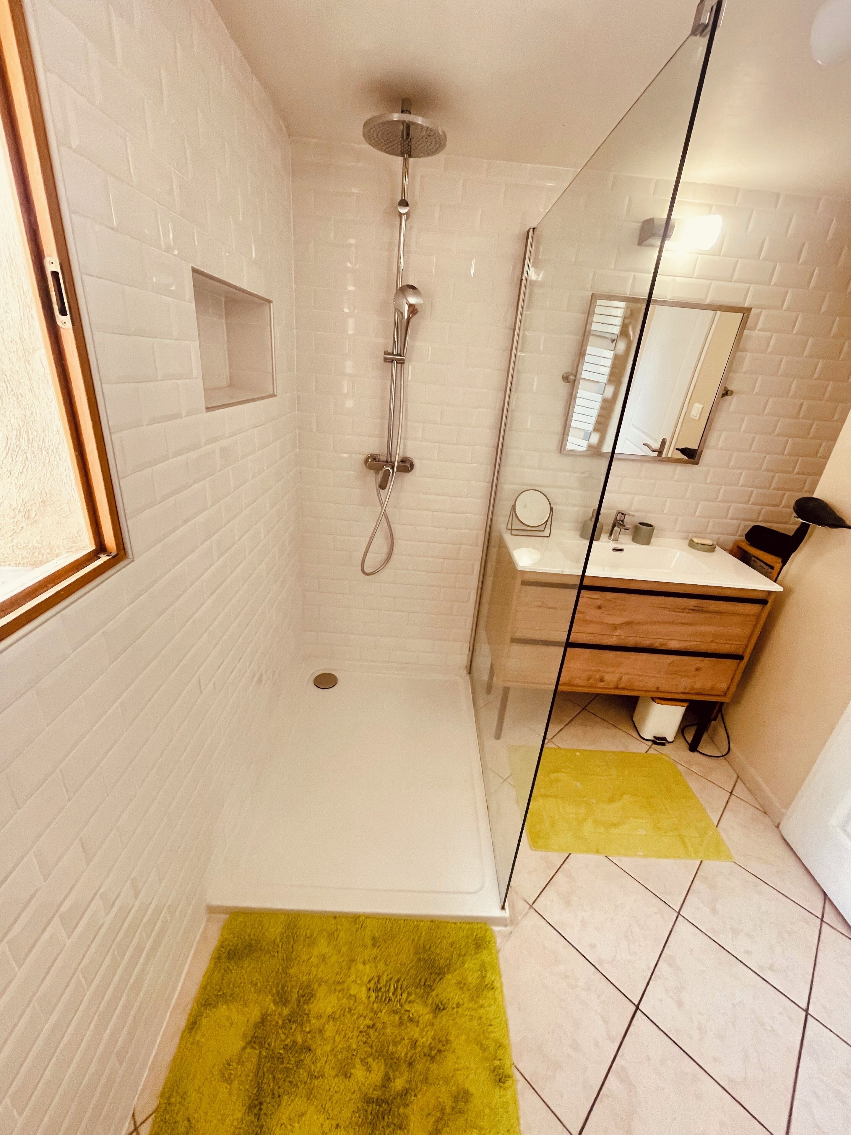 Un bagno moderno con box doccia in vetro, pareti piastrellate in bianco e un mobile lavabo in legno.