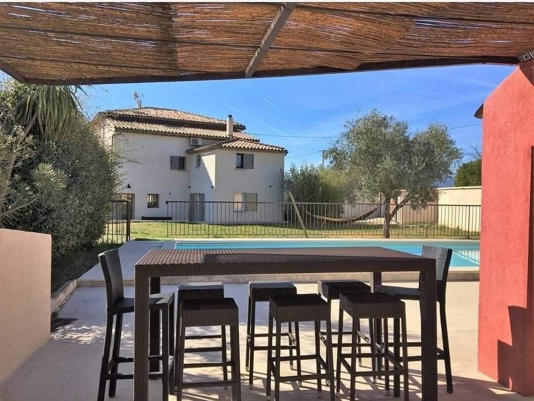 En uteplats med ett bord och stolar, en swimmingpool och ett hus i bakgrunden.