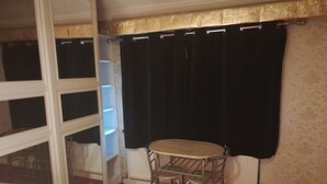 A room with a bed, a small round table with metal chairs, a window with black curtains, and a radiator. - Lovely 1-bed Studio in London (London)