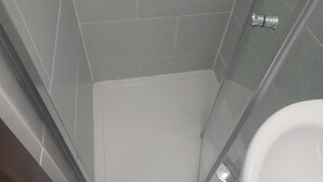 A modern bathroom with a glass shower enclosure, a white toilet, and grey tiled walls. - Lovely 1-bed Studio in London (London)
