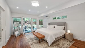 A modern bedroom with a large bed, a bench, a bedside table, and a view of the outdoors through glass doors.