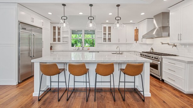 A modern kitchen with white cabinetry, a large island with bar stools, stainless steel appliances, and pendant lighting.