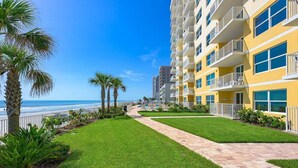Een hotel met een pad naar het strand, omringd door palmbomen en een verzorgd gazon.
