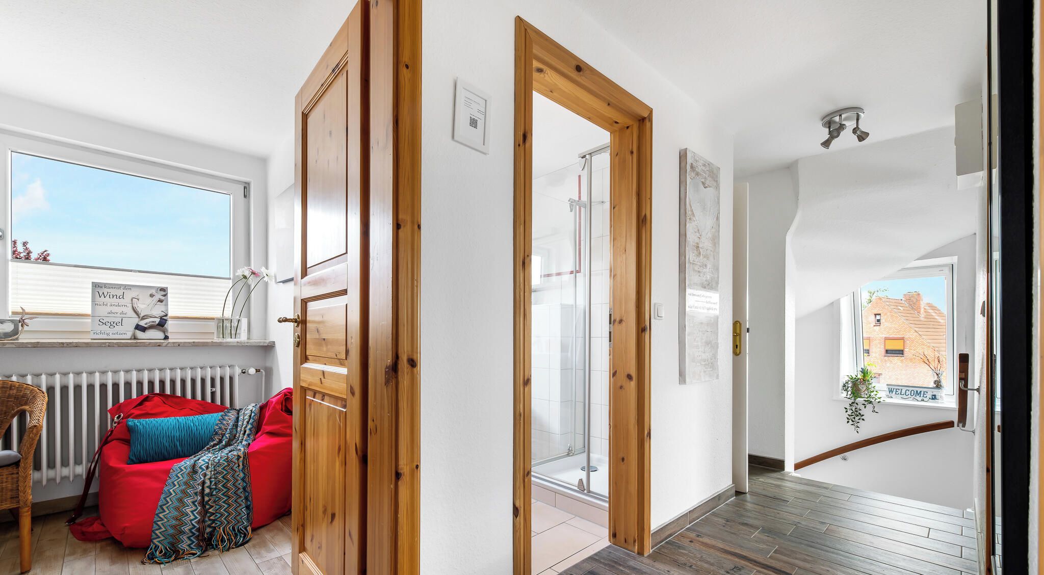 Un intérieur moderne avec un plancher en bois, un fauteuil en forme de sac de haricots rouge et une vue sur un bâtiment en briques à l’extérieur.