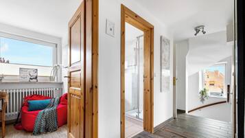 Een modern interieur met een houten vloer, een rode zakstoel en uitzicht op een bakstenen gebouw.