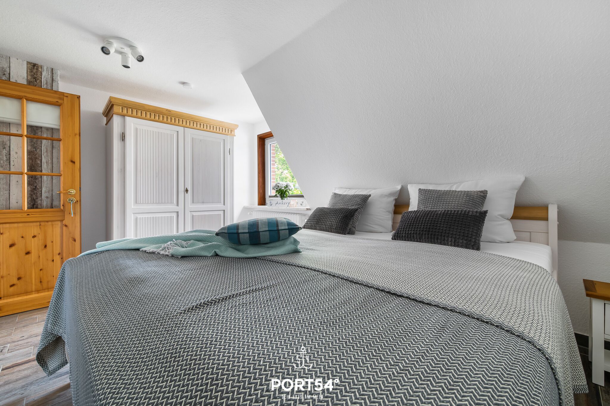 Een slaapkamer met een bed, kussens, een houten garderobe en een raam.