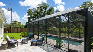 Une terrasse couverte avec une piscine, du mobilier d’extérieur et une vue sur le jardin arrière.