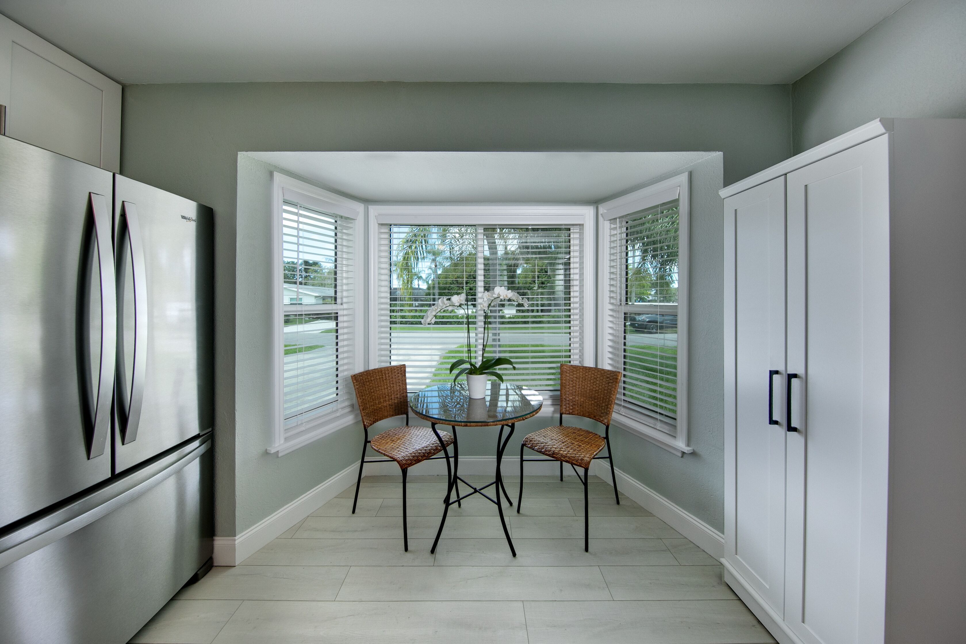 A kitchen with a refrigerator, a dining table with chairs, and a window with blinds.