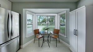 Une cuisine équipée d’un réfrigérateur, d’une table à manger avec des chaises et d’une fenêtre avec des stores.