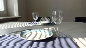 Une table à manger avec deux verres à vin et une assiette, placée dans une pièce dotée d’une fenêtre et recouverte d’une nappe à motifs.