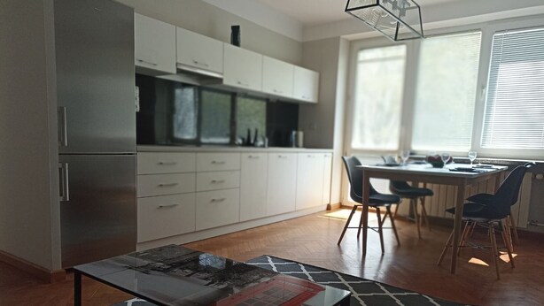 Une cuisine moderne avec des meubles blancs, un réfrigérateur en acier inoxydable et un coin repas comprenant une table et des chaises.