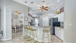 A modern kitchen with a central island, bar stools, and a ceiling fan. - Haven Hideaway with Saltwater Pool 3br Sleeps 8 (Sarasota)