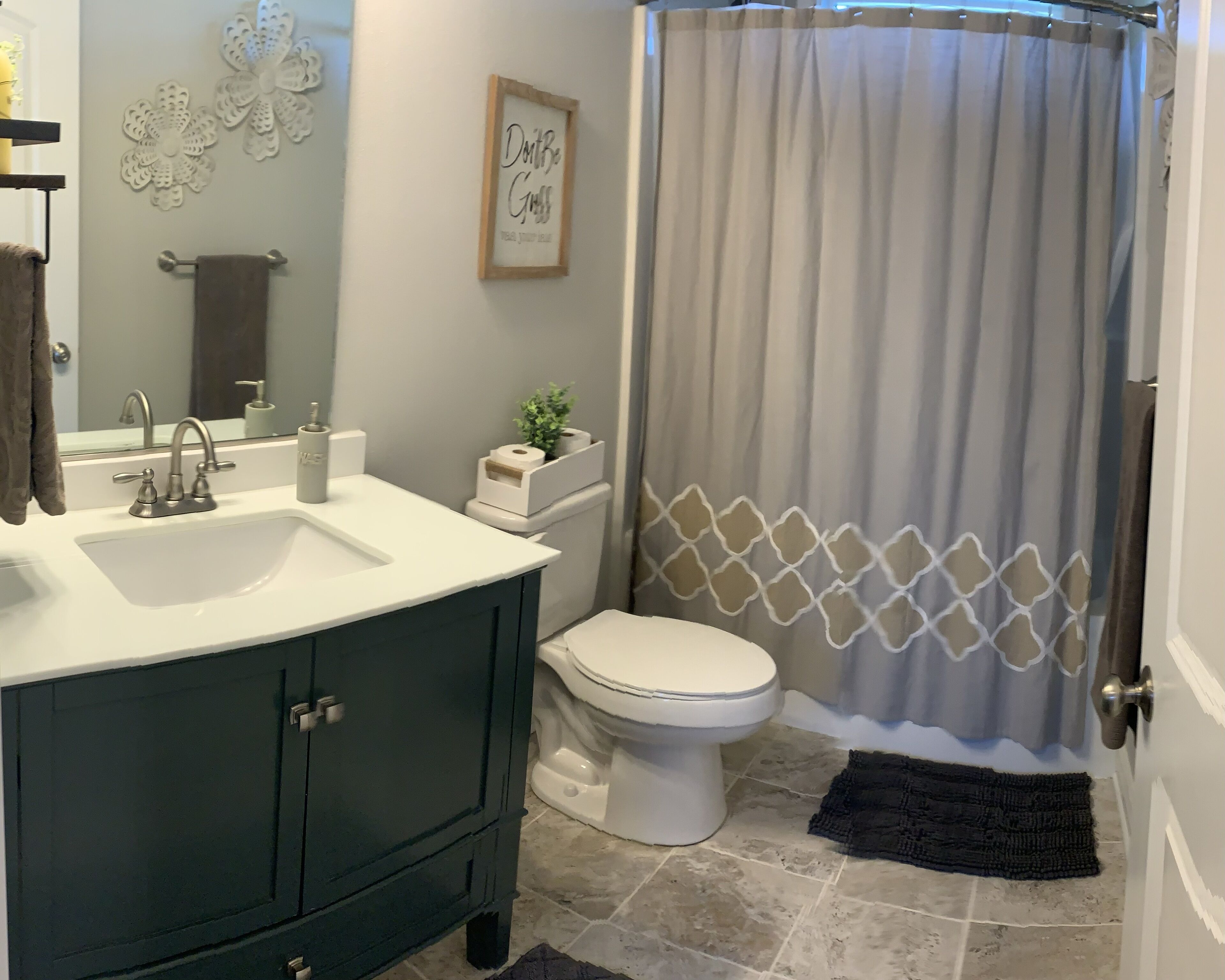 A bathroom with a white sink, dark green vanity, white toilet, and a shower curtain with a geometric pattern.