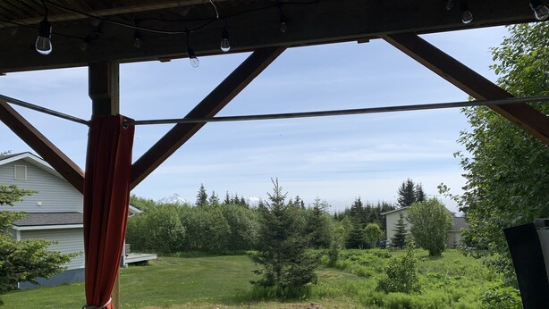 A hot tub with two legs submerged in water, set against a backdrop of a grassy yard and trees. - Daybreeze Vacation Home w/ Hot Tub & Gorgeous View (Homer)