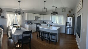 A modern kitchen with white cabinetry, a central island with bar stools, a stainless steel refrigerator, and pendant lighting. - Daybreeze Vacation Home w/ Hot Tub & Gorgeous View (Homer)