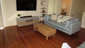 A living room with a flat-screen TV mounted on the wall, a light blue sofa with striped pillows, a wooden coffee table, and a wooden cabinet with a plant on top. - Lady Doris,  wifi  - Off Peak Special! (Port Vincent)