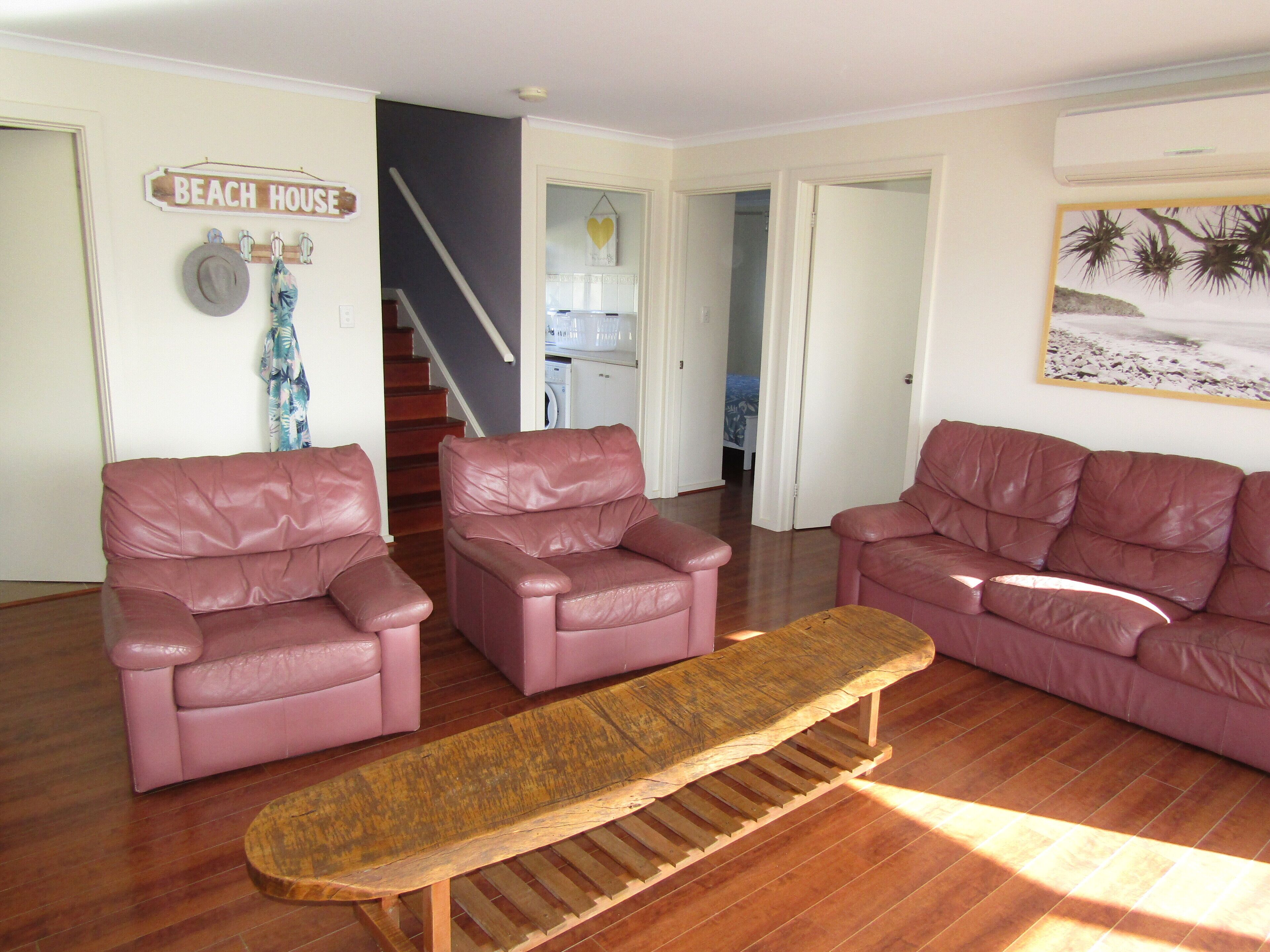 A living room with two pink leather sofas, a wooden bench, and a staircase leading to a kitchen.