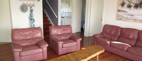 A living room with two pink leather sofas, a wooden bench, and a staircase leading to a kitchen.