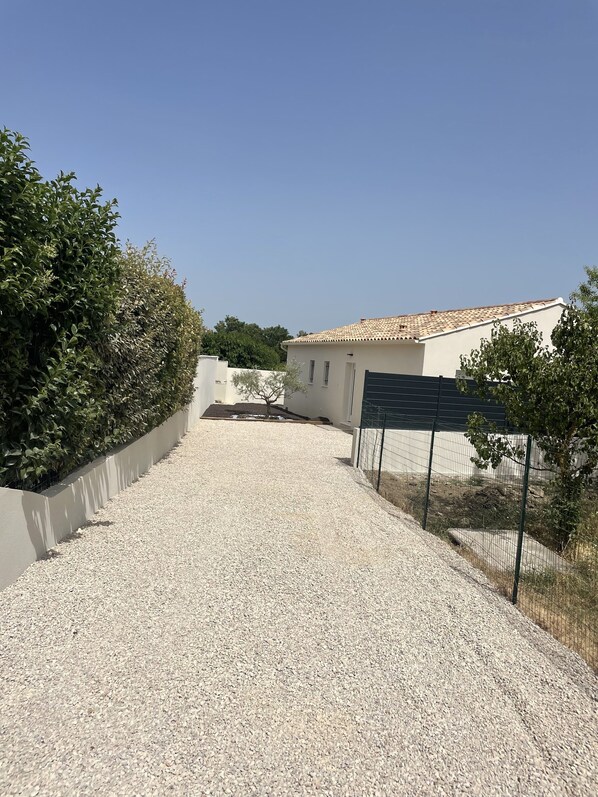 Uma entrada de cascalho leva a um edifício com telhado em telhas e uma parede branca.
