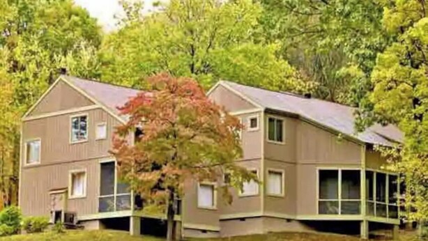 Ein zweistöckiges Haus mit geneigtem Dach, einer Veranda und einem Baum davor.