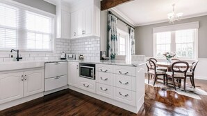 A modern kitchen with white cabinetry, a built-in microwave, and a dining area with a wooden table and chairs. - 3BR Family Home Sleeps 6 – Fireplace, Spa Bath, Near Blue Lake | Ideal for Extended Stays (Mount Gambier)