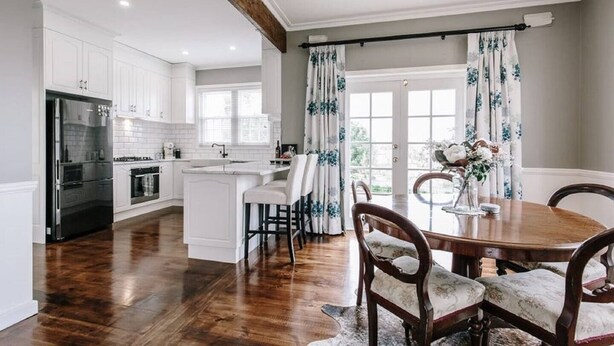 A spacious kitchen with white cabinetry, a central island, and a dining area with a wooden table and chairs. - 3BR Family Home Sleeps 6 – Fireplace, Spa Bath, Near Blue Lake | Ideal for Extended Stays (Mount Gambier)