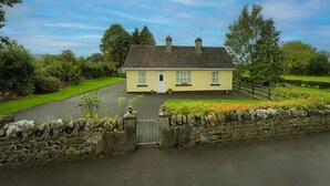 A two-story house with a stone wall entrance, a paved driveway, and a well-maintained lawn.