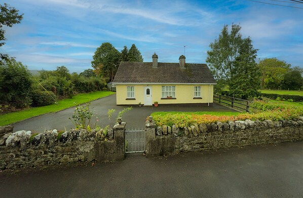 A two-story house with a stone wall entrance, a paved driveway, and a well-maintained lawn.