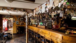 A bar with a wooden counter, stools, and a wall covered in various papers and notes.