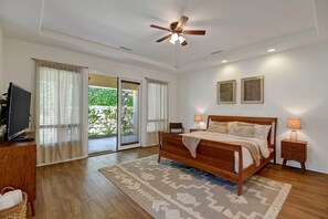 A bedroom with a wooden bed, a ceiling fan, a television, and a large window with curtains.