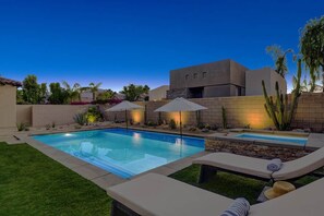 Un patio trasero con piscina, sillas de descanso y una casa moderna.
