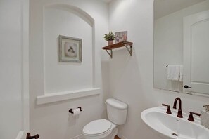 Un baño con inodoro blanco, lavamanos con espejo y un pequeño estante con una planta.