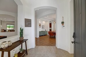 A modern interior with a wooden floor, a dining area with chairs, a kitchen with cabinets, and a grey door.