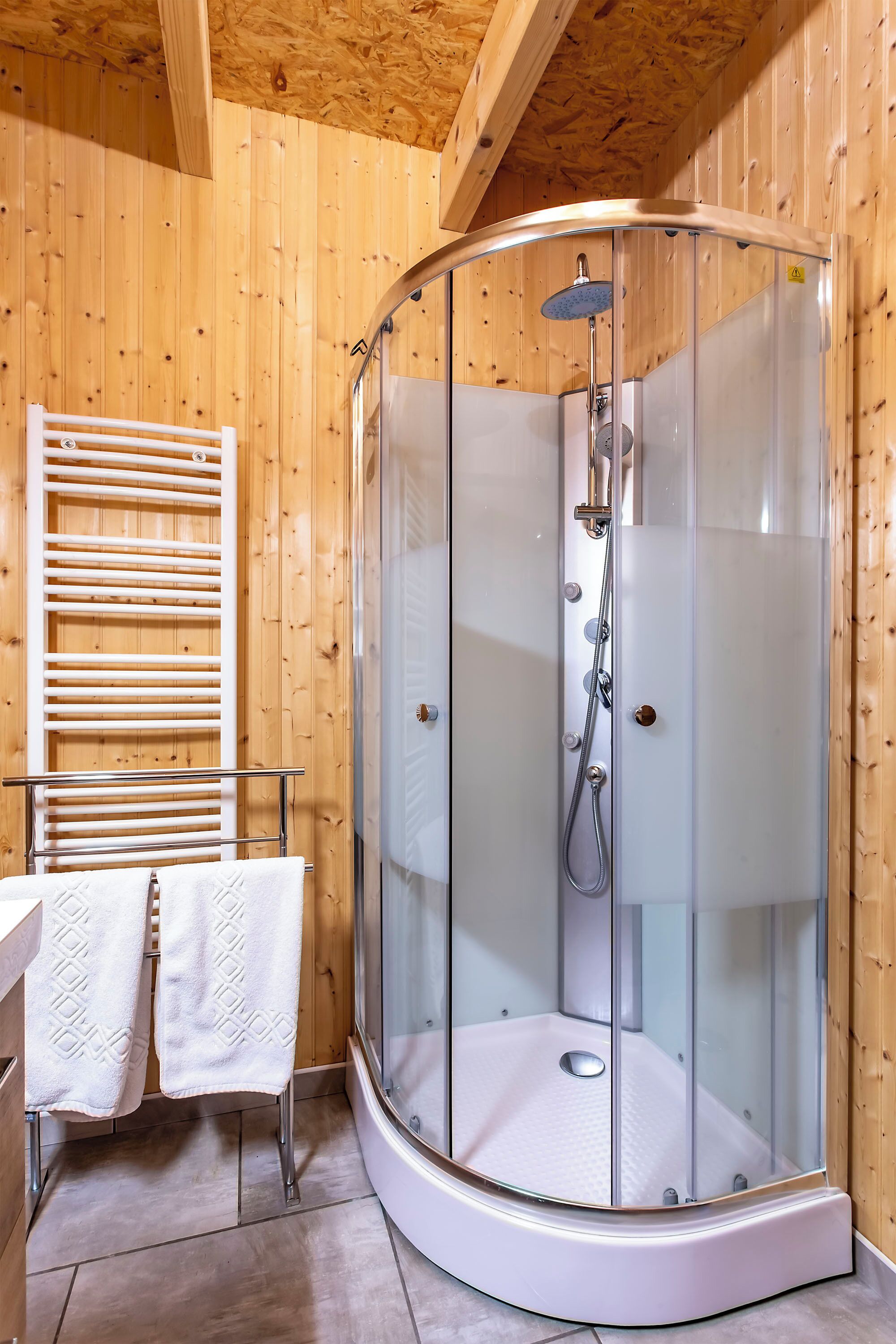 A modern shower enclosure with a glass door, a white towel rack, and a wooden interior.