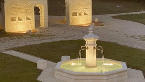 Ein Steingebäude mit Rundbogenportal und einem Brunnen davor.