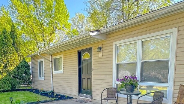 Une maison de plain-pied avec un porche à l’avant, un petit jardin et une terrasse avec deux chaises et une table.