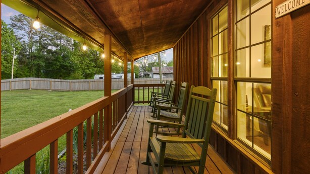 A covered porch with wooden railings, a "WELCOME" sign, and several green Adirondack chairs. - 2Br Cabin with hot tub, BBQ, 55" Smart TV, W/D. (Broken Bow)