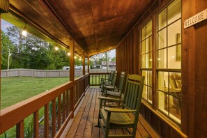 Een overdekt terras met houten reling, een 'WELCOME'-bord en meerdere groene Adirondack-stoelen.