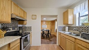A kitchen with wooden cabinets, a central island, and a dining area with chairs. - 2Br Cabin with hot tub, BBQ, 55" Smart TV, W/D. (Broken Bow)