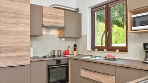 A modern kitchen with wooden cabinets, a built-in oven, a microwave, and a window with a view of greenery.