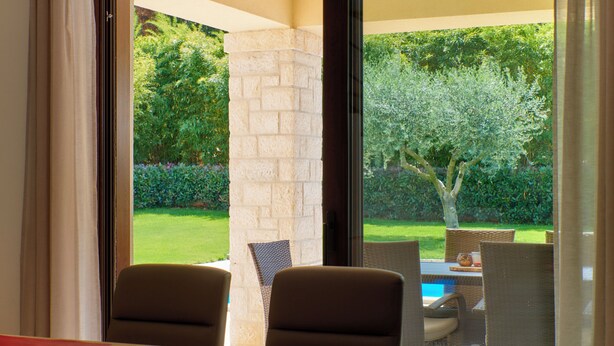 A room with a dining table and chairs, a large window with a view of a garden and a tree.